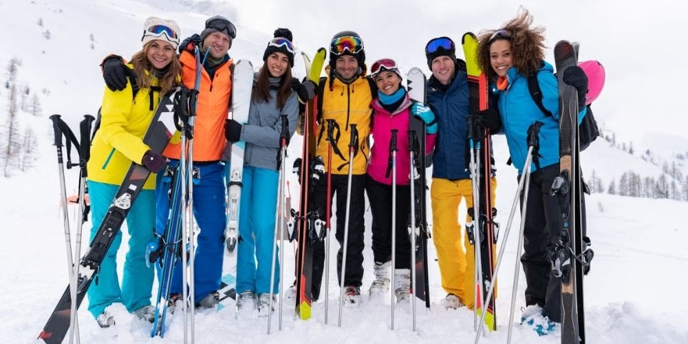 Group of friends standing together on a snowy mountain holding skis, smiling after a day of winter adventure.