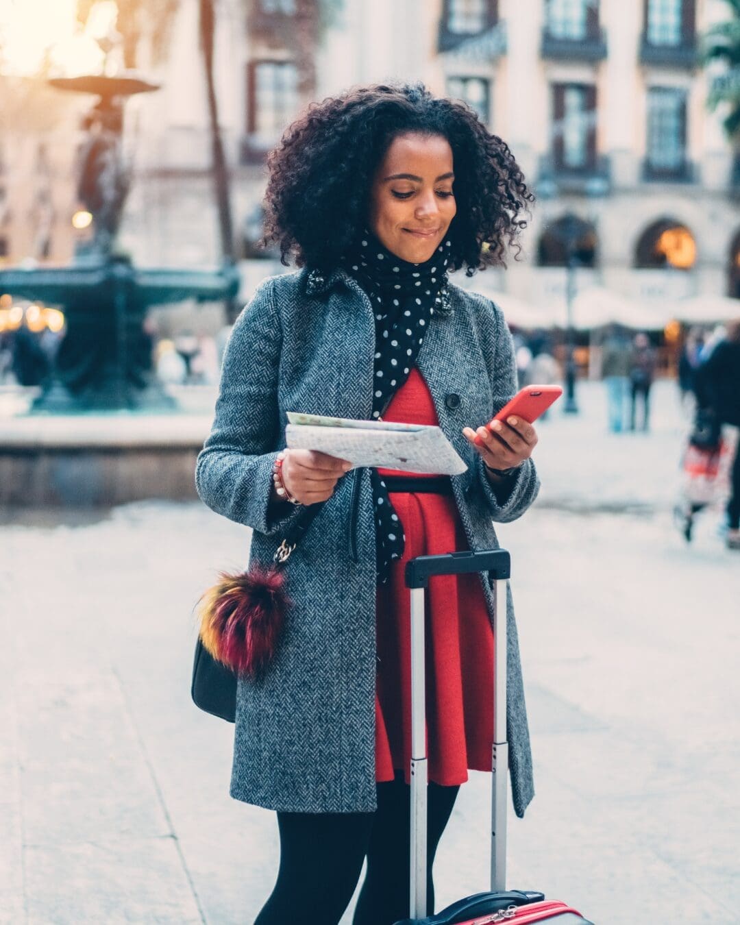 Solo traveler using a smartphone and map while exploring a city with rolling luggage.