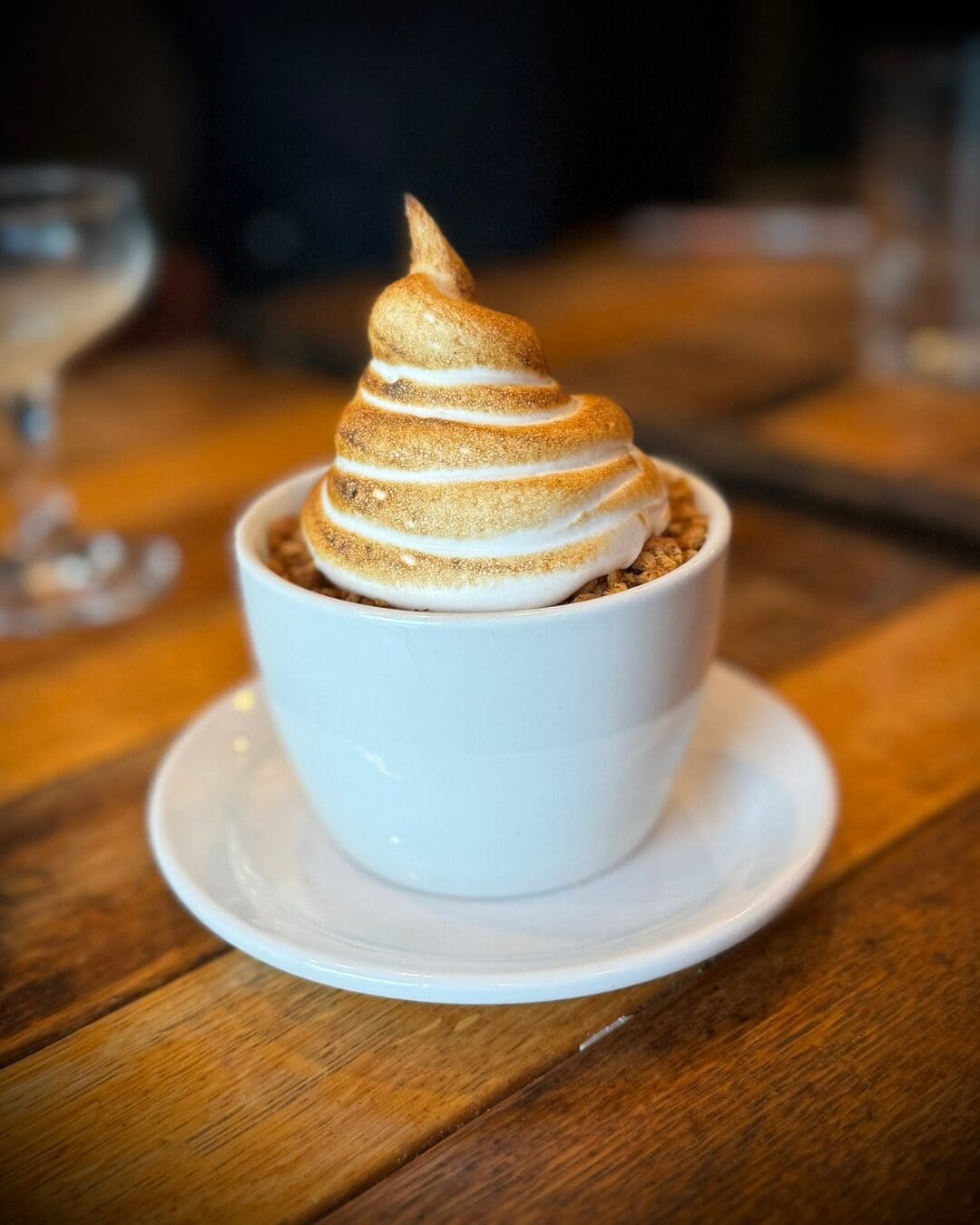 Toasted meringue-topped dessert served in a white cup at a restaurant.